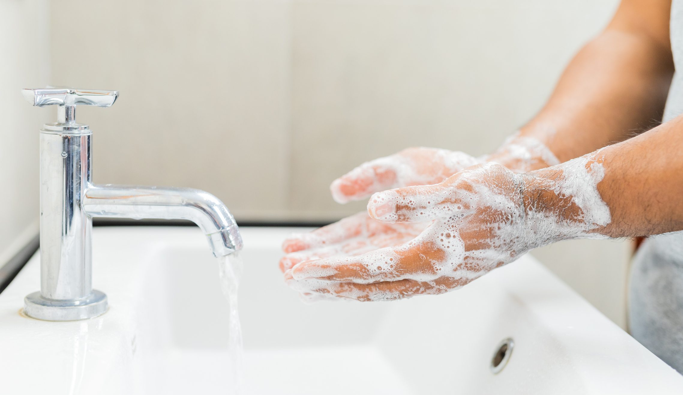 cropped shot of man washing his hands in bathroom sink