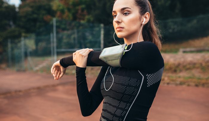 Portrait of a beautiful sports woman stretching hands outdoors. Caucasian female warming up.