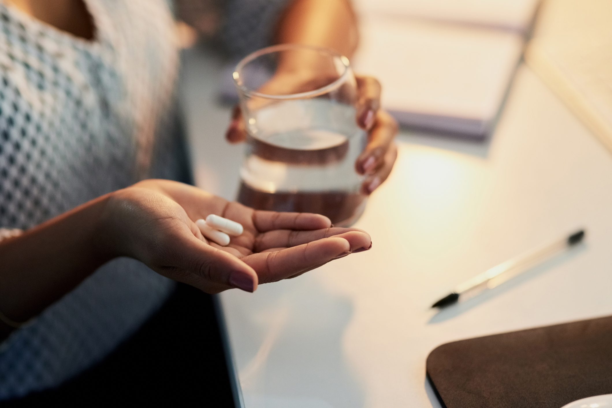 close up of woman holding pain pills and glass of water at night