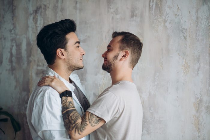 Hot gay couple at the sweet moment of love enjoying closeness and passion kissing isolated over grey lounge rustic background