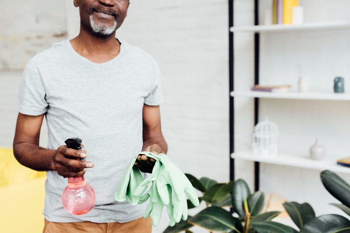close up of african american man holding rubber gloves and spray