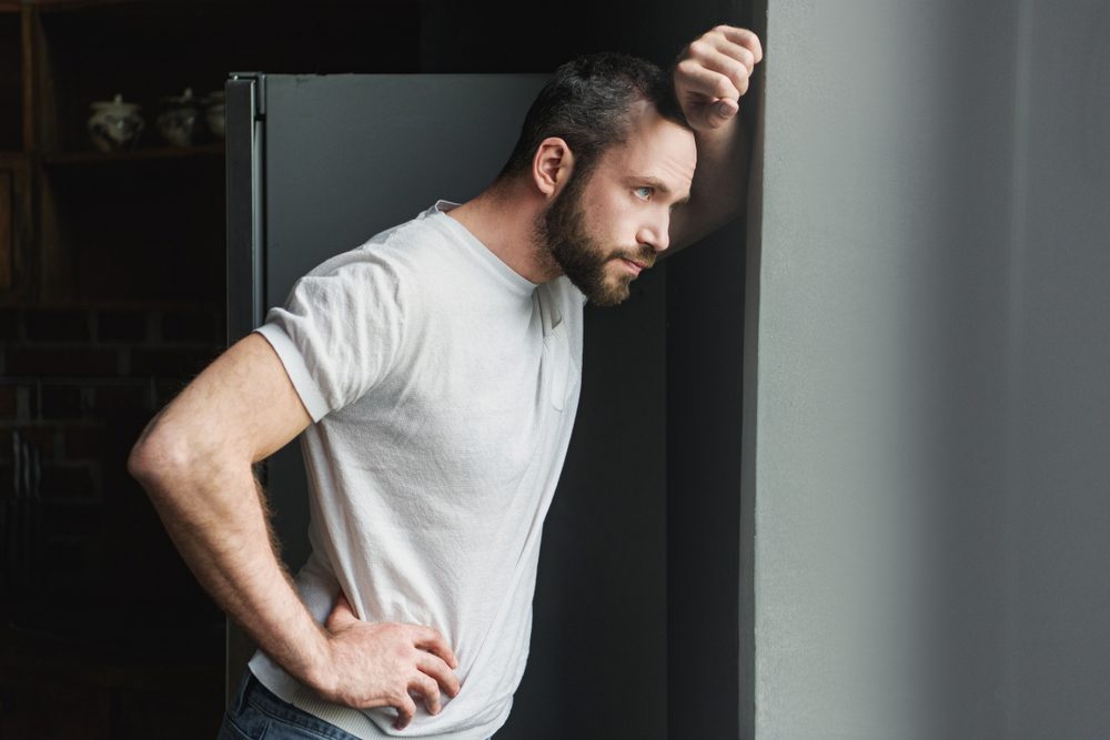 side view of depressed young man leaning on wall and looking away