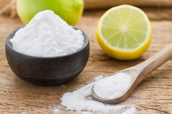 baking soda in a wooden bowl with a wooden spoon, and lemon on a wooden surface