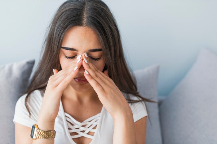 Sad woman with brown hair holding her nose and head, which hurts from sinus pain.