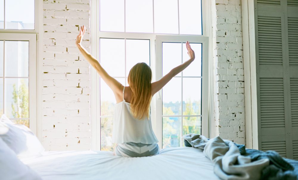 Woman stretching in bed after waking up, back view, entering a day happy and relaxed after good night sleep. Sweet dreams, good morning, new day, weekend, holidays concept