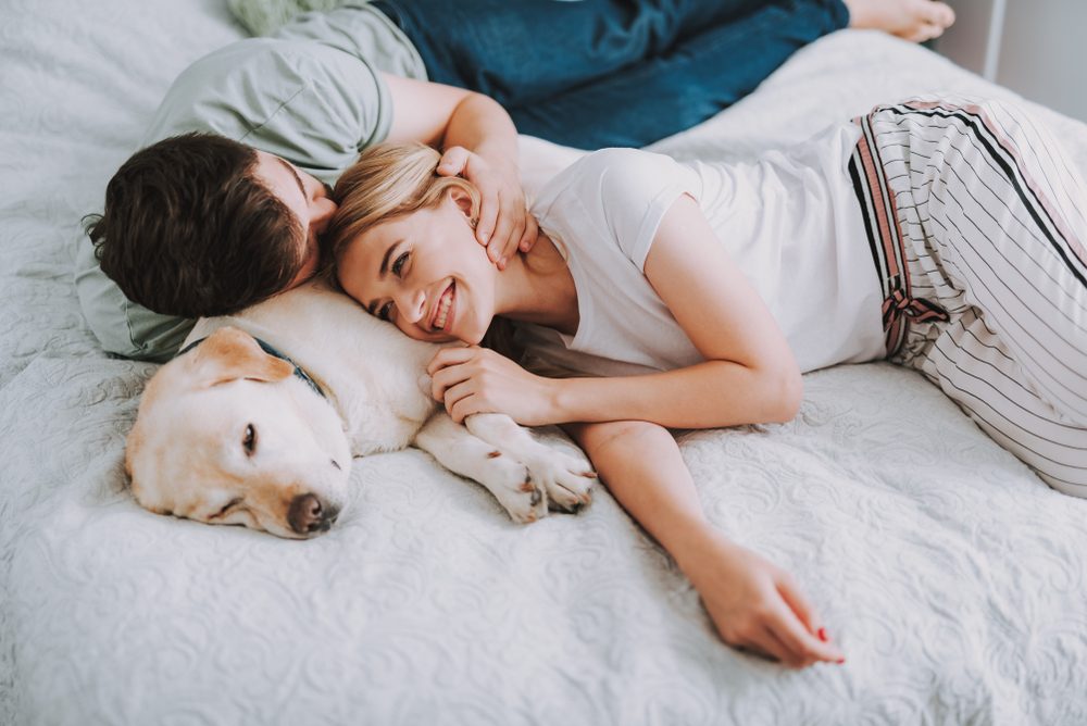 Pleasant young couple having rest in bed while their dog sleeping nearby