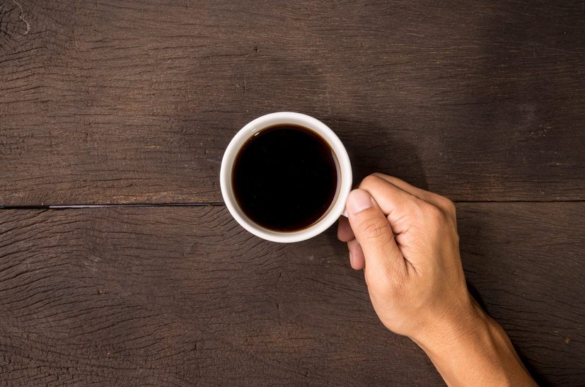 Male hand hold mug of espresso coffee on wood table.