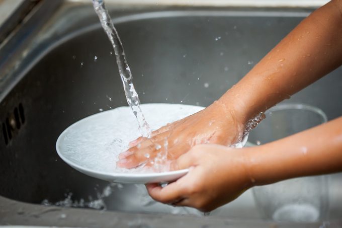 Child hand washing dishes over the sink in the kitchen