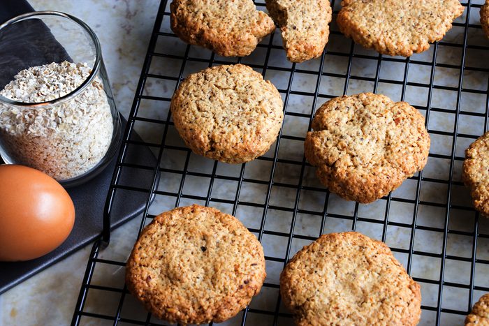 Glutenfree homemade oatmeal cookies on a cooling rack alongside a cup of oats and an egg.