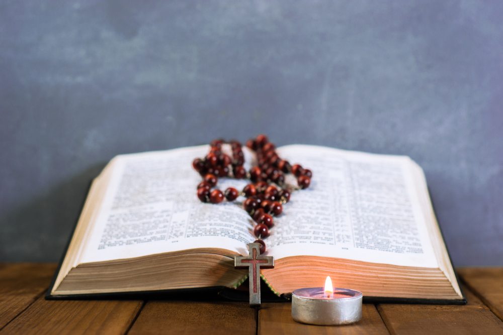 Bible crucifix and beads with a candle on a brown wooden table. Beautiful background.Religion concept.