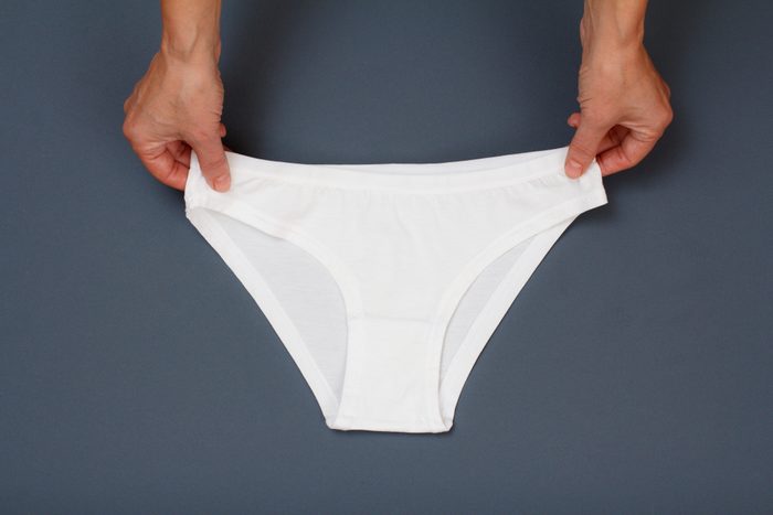 Women's hands holding white cotton panties on gray background. Woman underwear set. Top view.