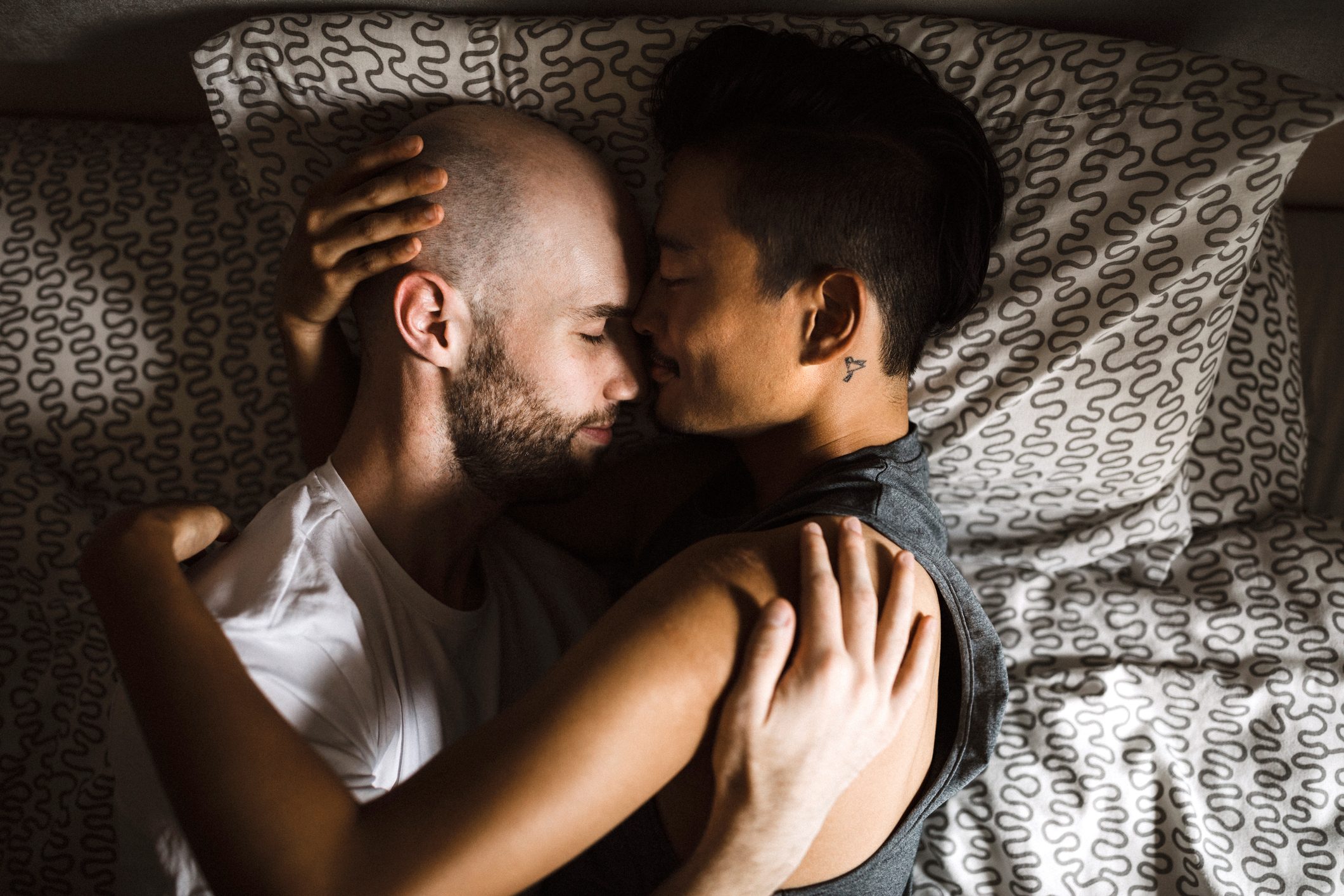 gay couple laying in bed together embracing