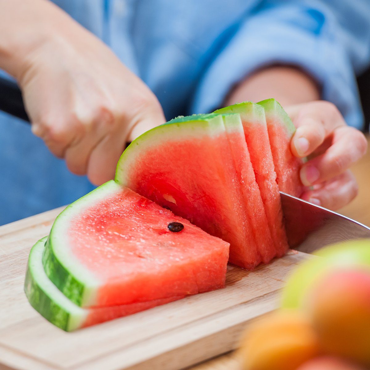 woman cutting watermelon into pieces on a wooden board