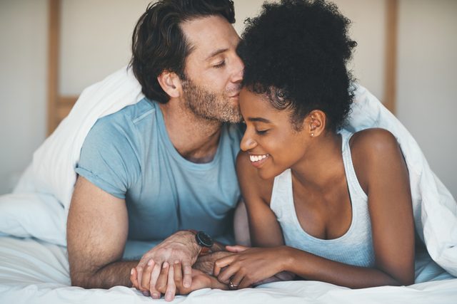 man kissing woman on her forehead in bed