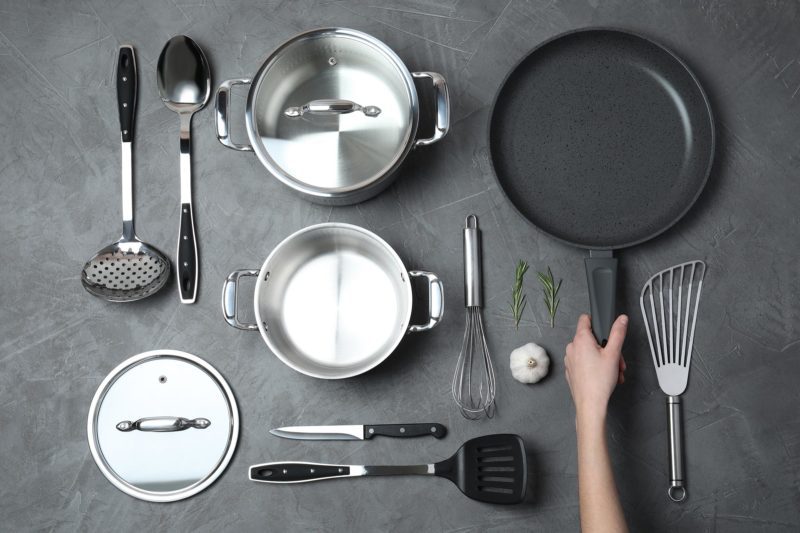 Woman holding frying pan over table with clean cookware, top view