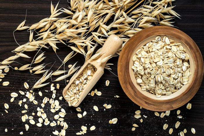 Oat stems and oat flakes in a wooden pot on a dark background. Top view