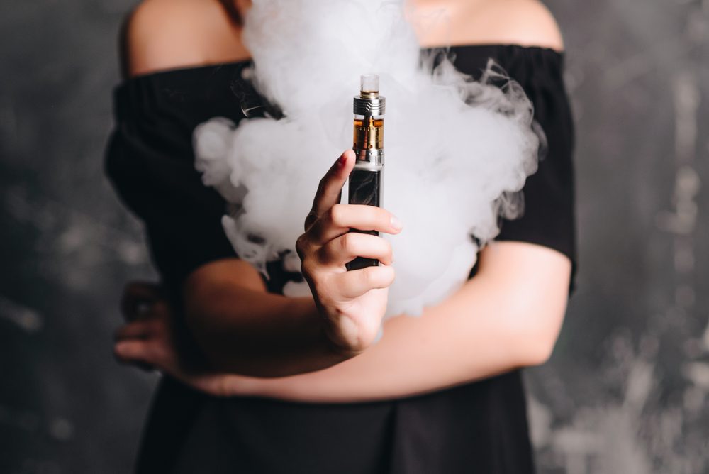 Close-up photo of female holding e-cigarette with smoke. Indoors