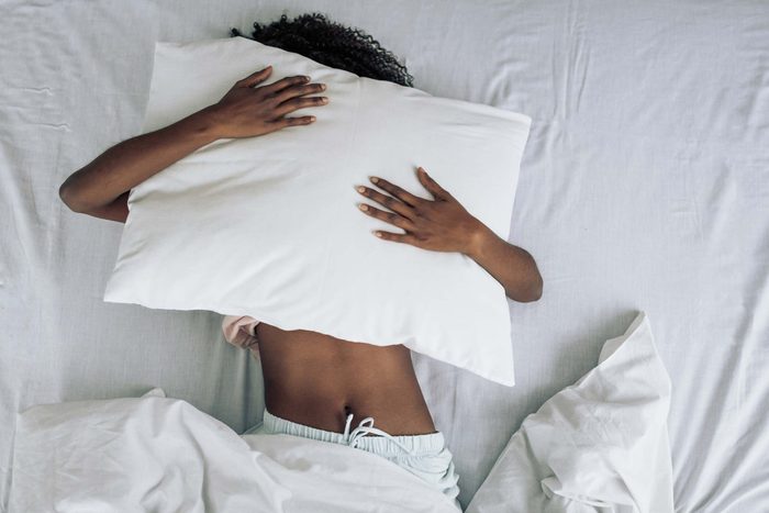 tired girl bed holding a pillow over her face