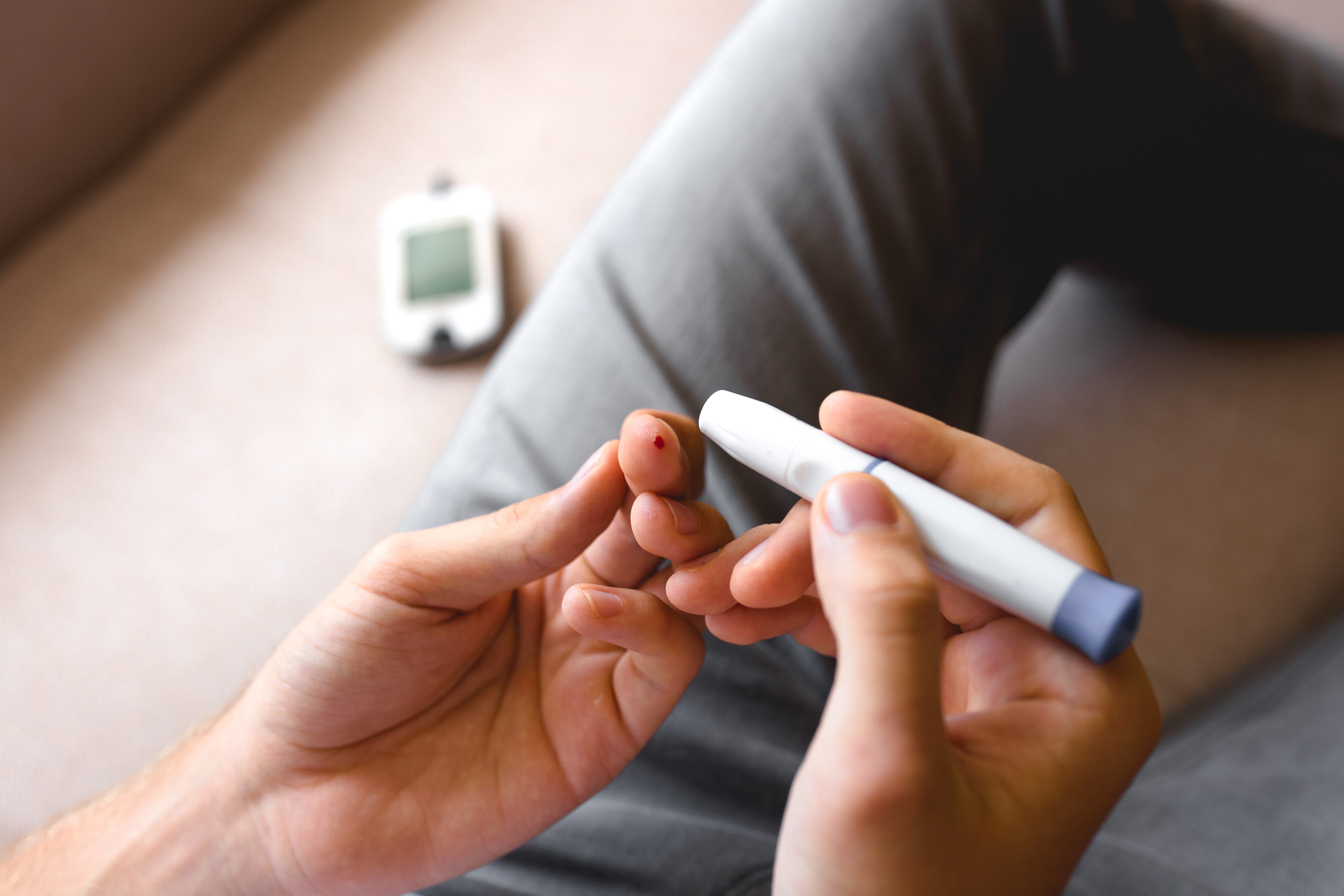 Handsome stylish young teen caucasian white brunette guy man european taking a blood sample with a glucometer to measure sugar level,lancet on finger diabetes, glycemia meter top first view shot