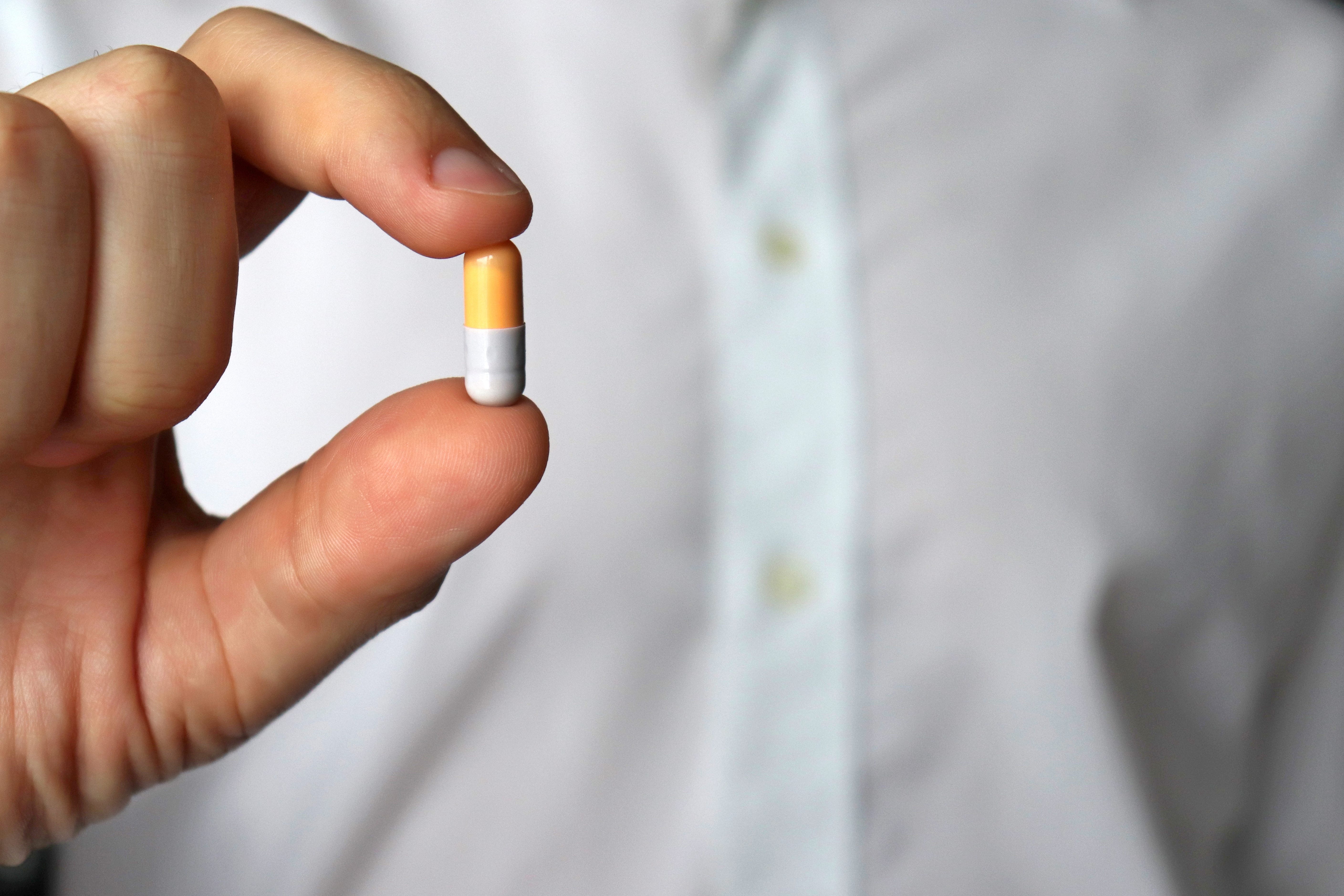 Doctor holding pill, male hand with medication in capsule close-up. Man with tablet, concept of pharmacist, drugs, diet pill, antidepressant or vitamins