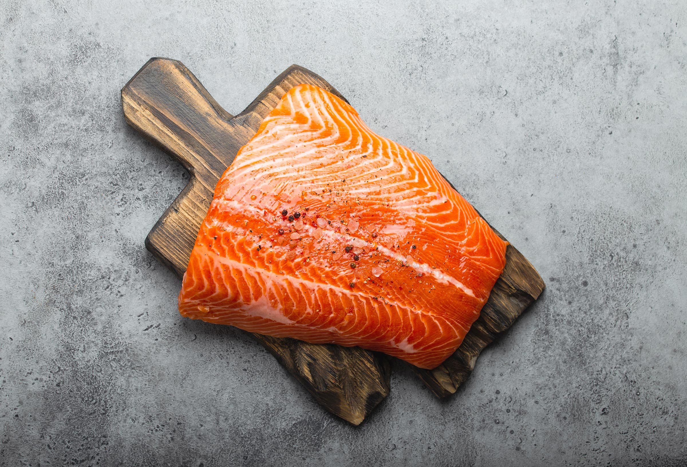 whole fresh raw salmon fillet with seasonings on wooden board