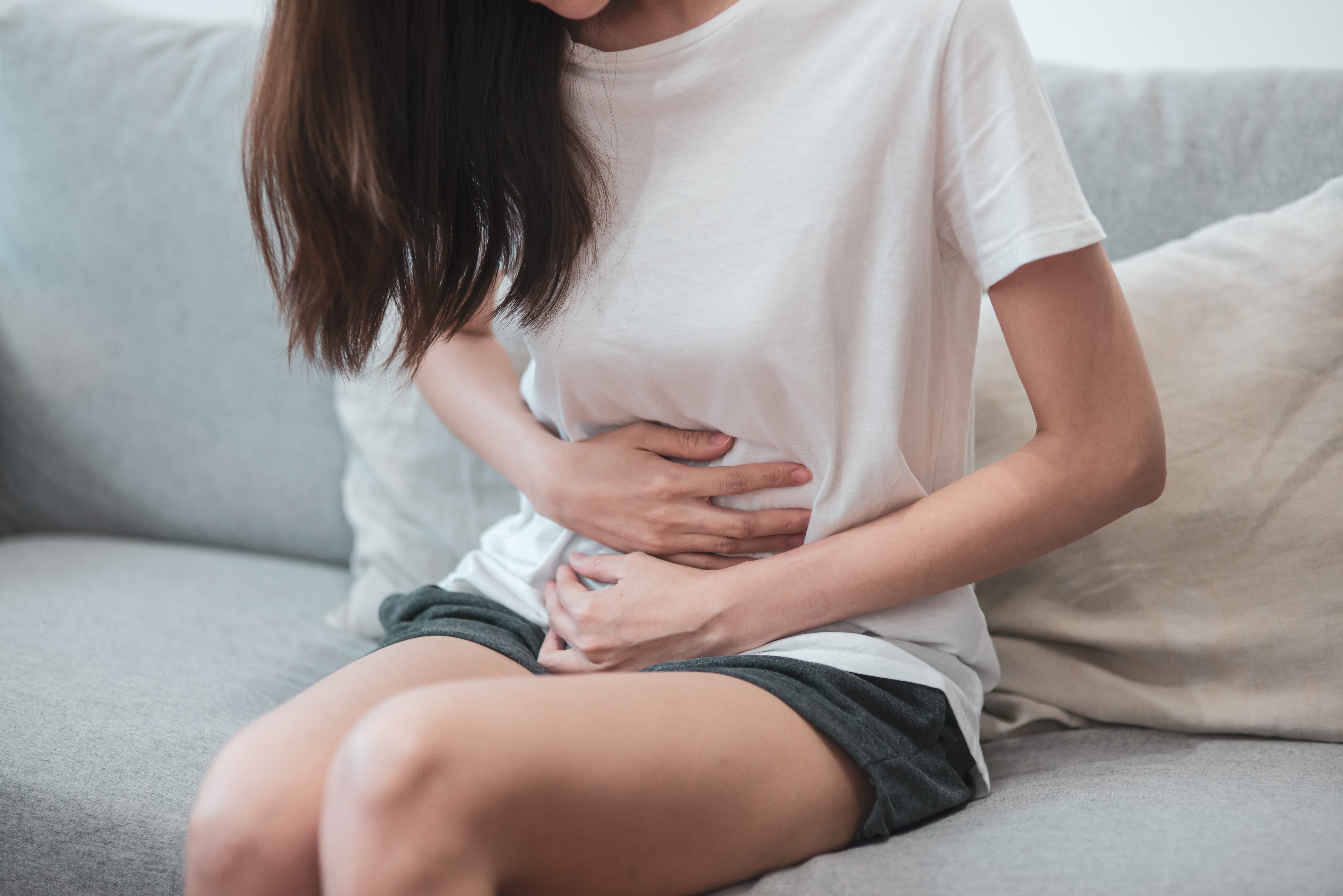 Healthcare medical or daily life concept : Close up stomach of young lady have a stomachache or menstruation pain sitting on a sofa.