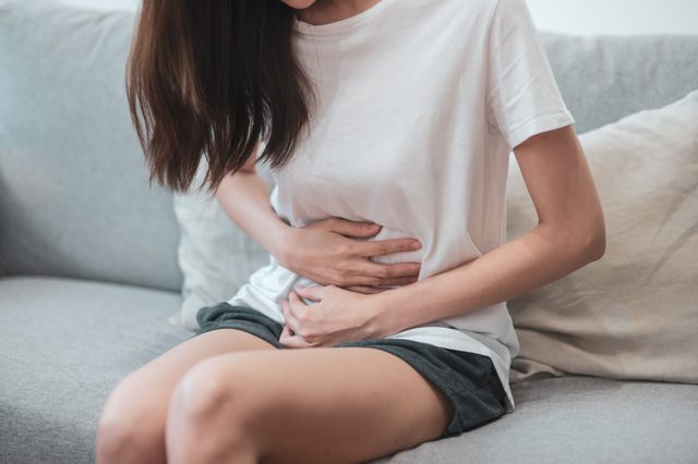 Healthcare medical or daily life concept : Close up stomach of young lady have a stomachache or menstruation pain sitting on a sofa.