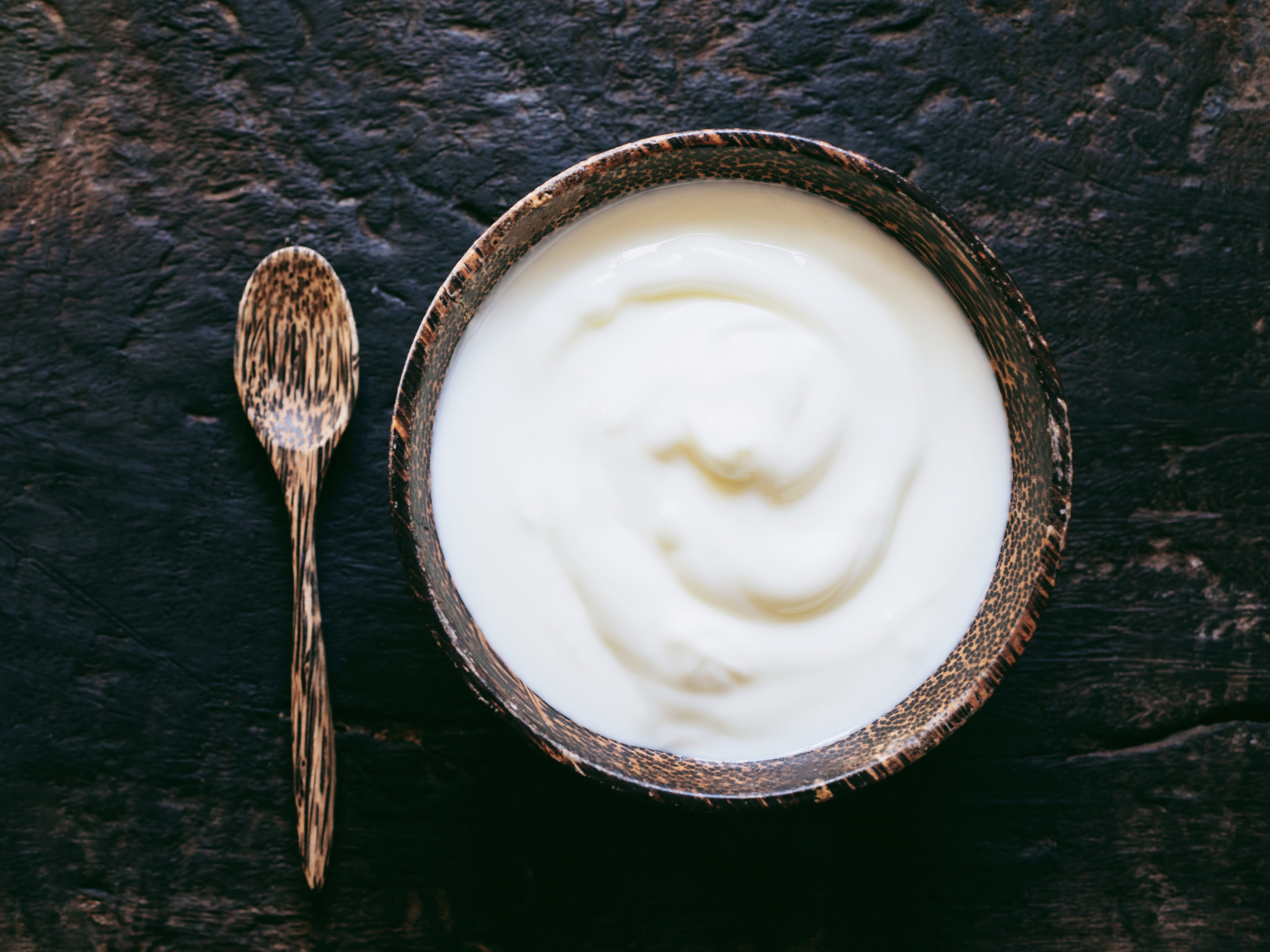 Greek yogurt or sour cream in a wooden bowl on dark table top view. Healthy food nutrition.