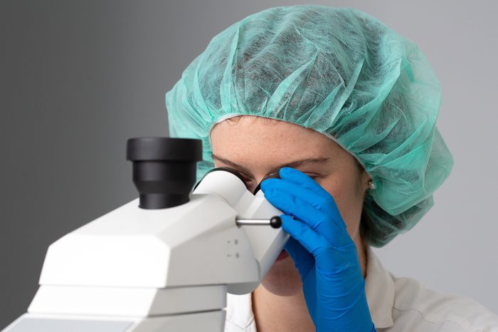 A pretty girl scientist is seen up close, looking through a professional microscope inside a biochemistry laboratory, with room for copy.