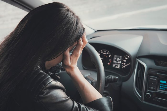 Stressed woman driver sitting inside her vehicle. Brunette girl doing face palm being at car wheel and dashboard background. Female driver is frustrated because of car accident. Headache and sickness