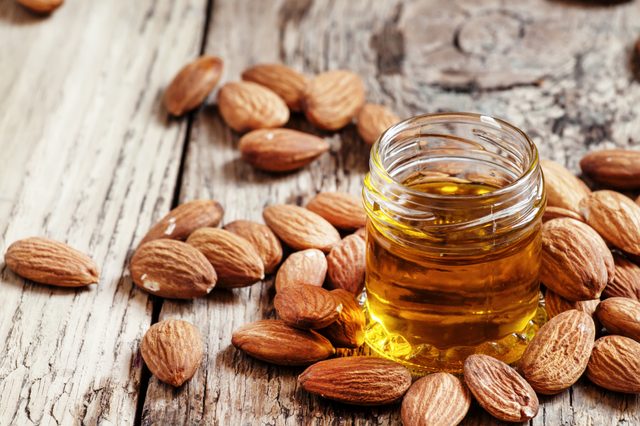 Sweet Almond Oil, first extraction, in a small glass jar, dry almond nuts on an old wooden background, selective focus