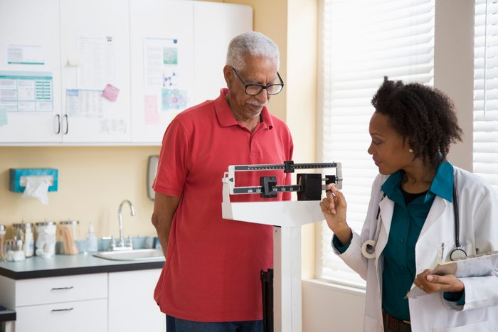 senior man standing on weight scale at the doctor