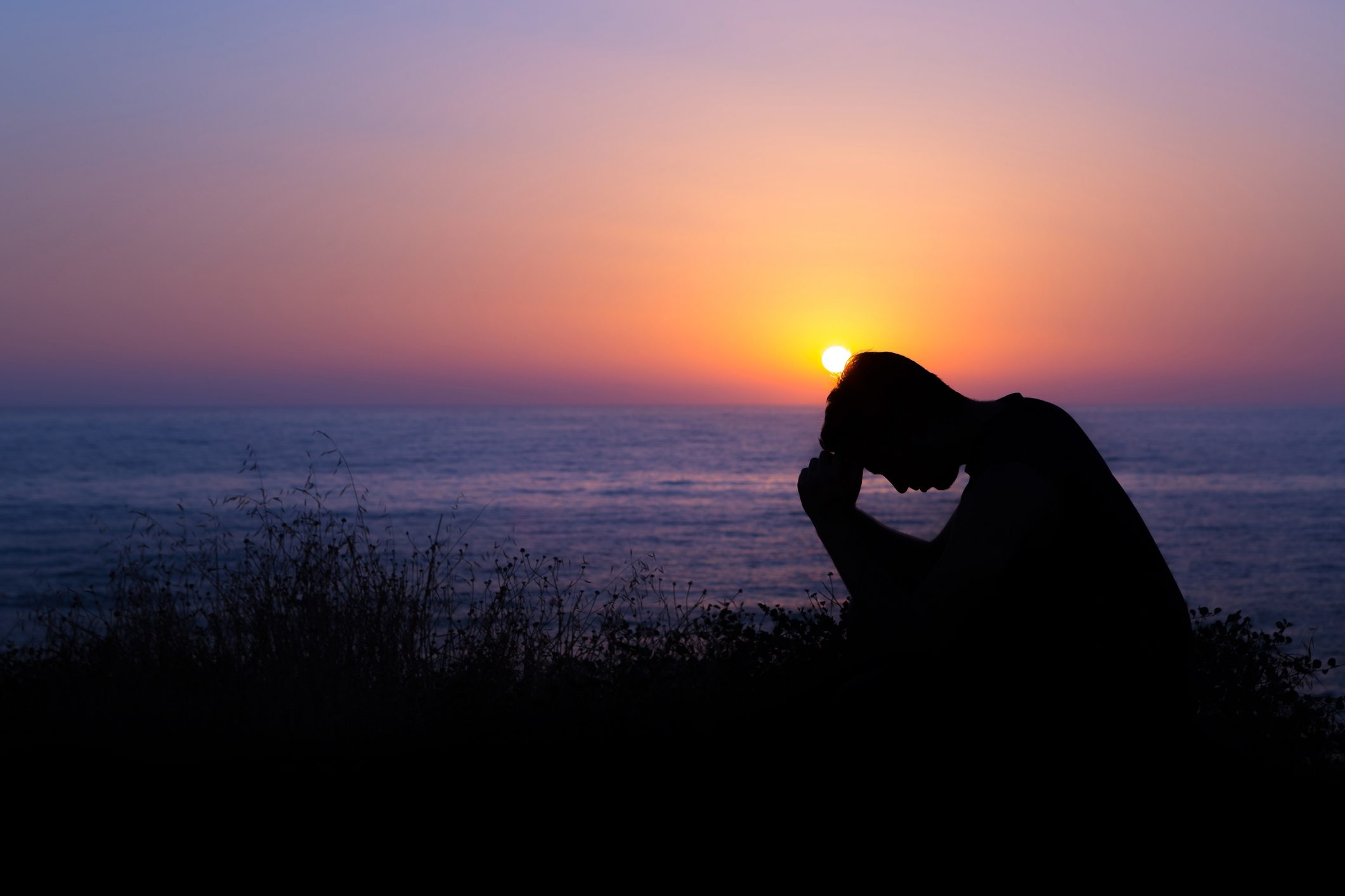 silhouette of sad man sitting on the beach during sunset