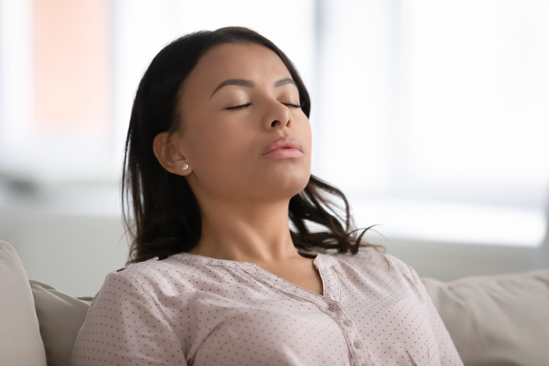 woman taking a deep breath while sitting on couch at home