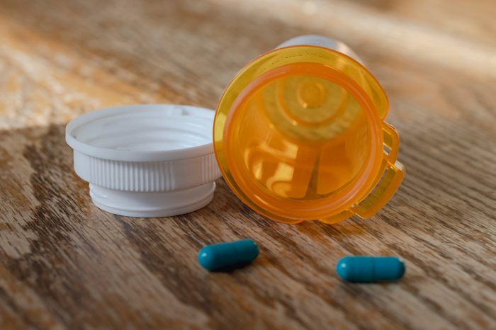 Prescription pill bottle with last two blue pills spilling onto wooden kitchen table. Close up view.