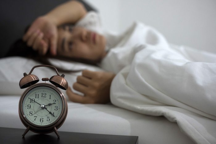 woman lying in bed with clock on night table