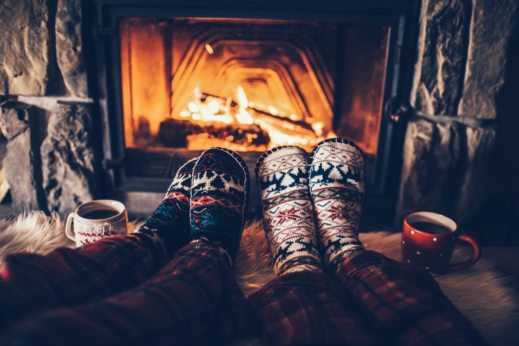 Feet in woollen socks by the Christmas fireplace. Couple sitting under the blanket, relaxes by warm fire and warming up their feet in woollen socks. Winter and Christmas holidays concept.