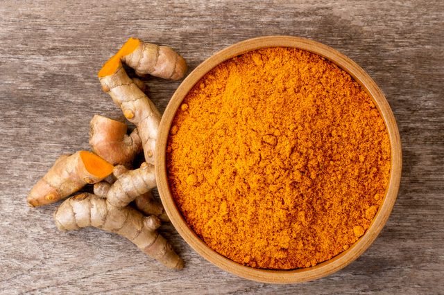 Turmeric powder in wooden bowl and tumeric root isolated on rustic wood table background. Top view.  