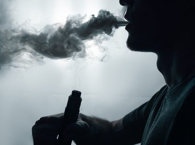 male vapor silhouette exhales a cloud of smoke using an electronic cigarette . copy space