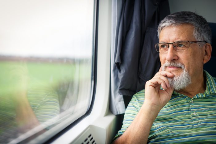 Senior man enjoying a train travel - leaving his car at home, he savours the time spent travelling, looks out of the window, has time to admire the landscape passing by