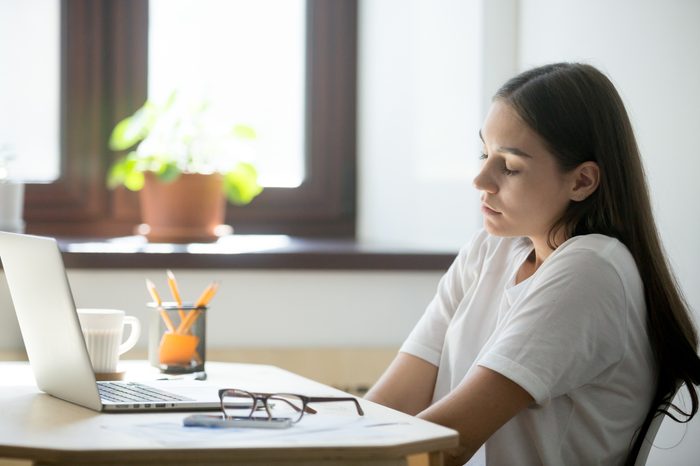 Female employee relaxing in her workplace, stretching her shoulders and back, keeping eyes closed . Woman taking a minute break from work, sitting near office window.