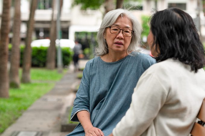 two women sitting on a park bench having a serious conversation