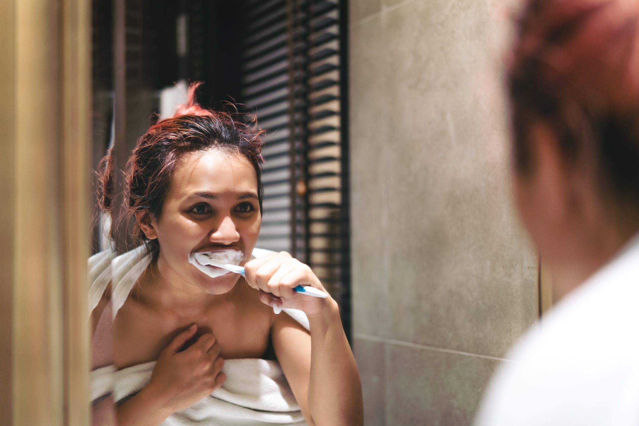 woman brushing teeth and looking in mirror