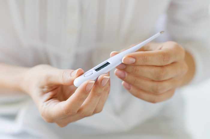 woman holding a thermometer taking her temperature