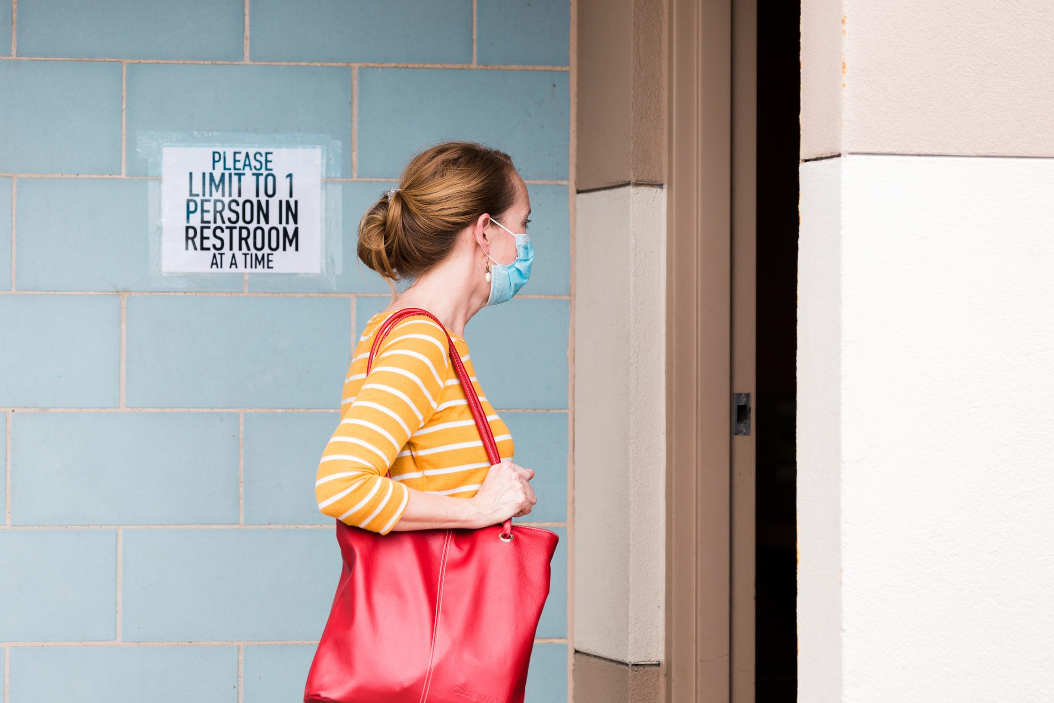 woman wearing face mask walking into public restroom