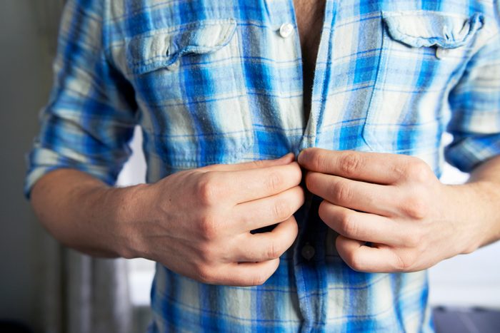 man buttoning shirt close up