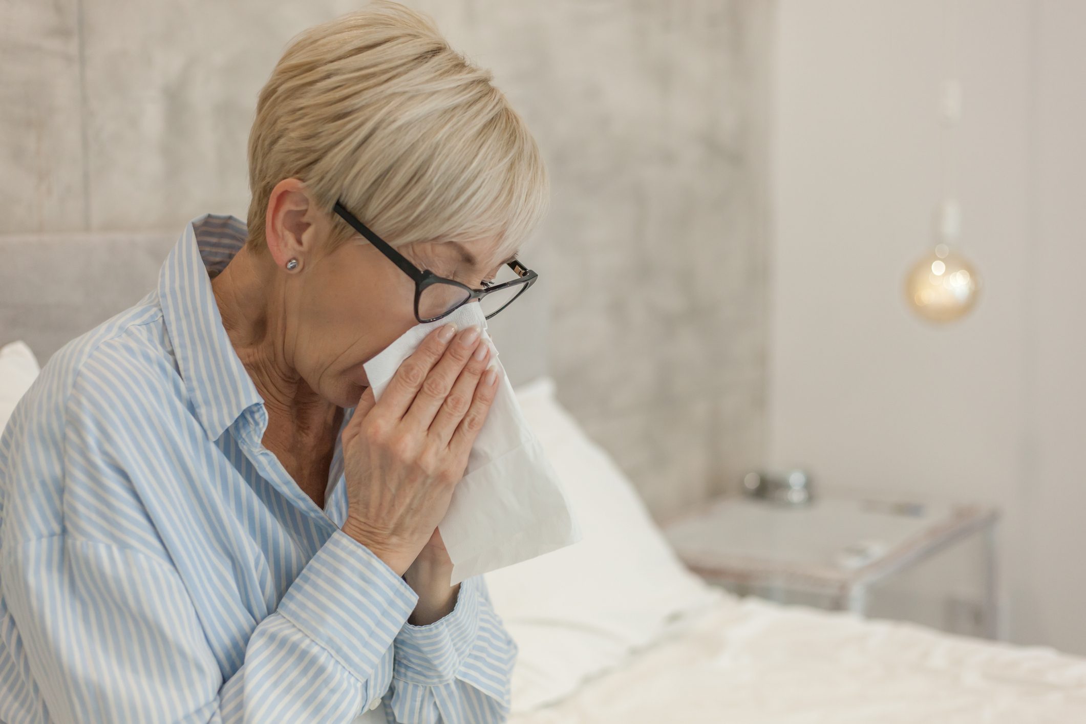 Close-Up Of Woman Sneezing While Sitting On Bed At Home