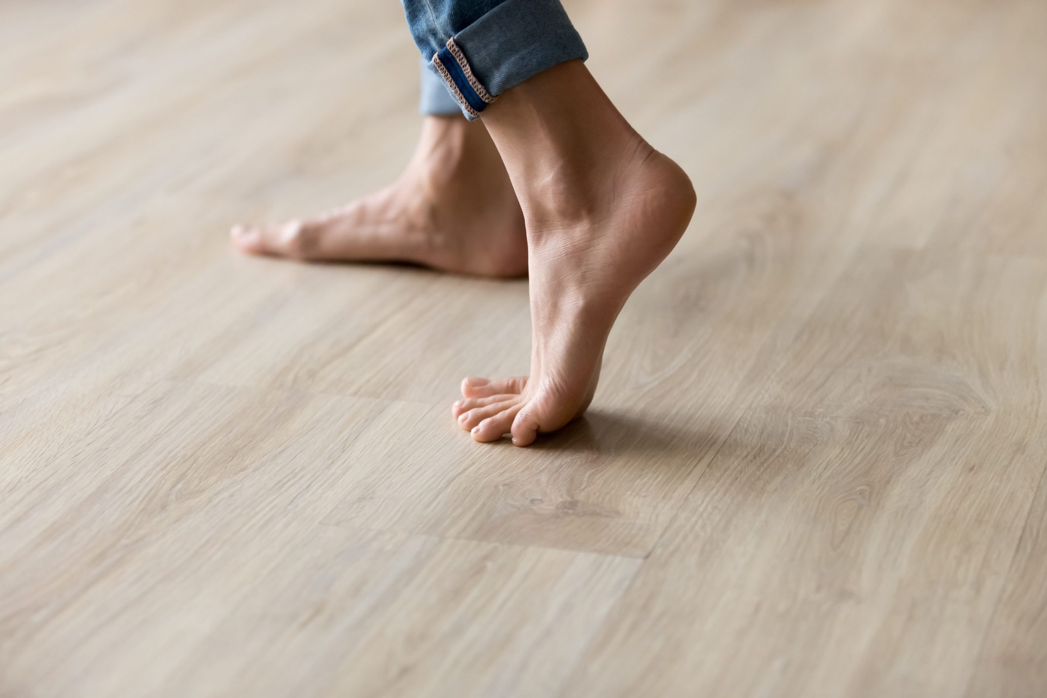 Side closeup view woman feet stands on warm wooden floor