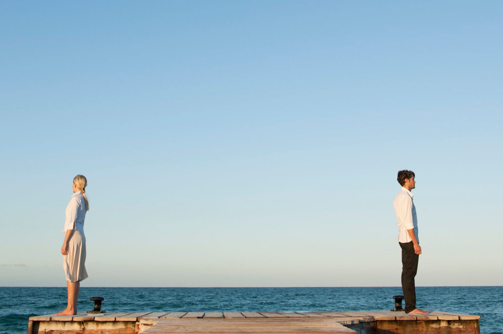 couple standing back to back near ocean
