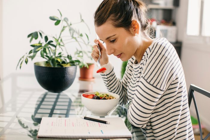 Woman sitting at table with fruit muesli looking at notepad